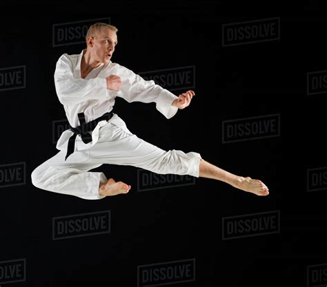 Young Man Performing Karate Kick On Black Background Stock Photo