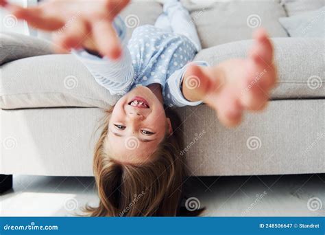 Lying Upside Down On The Sofa Cute Little Girl Indoors At Home Alone