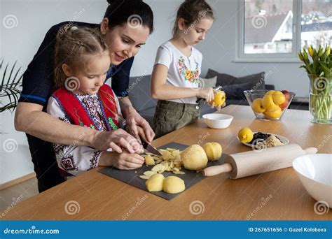A Mother And Two Daughters Cook Apple Pie Filling Together At The Table A Mother Teaches Her