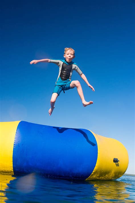 Boy Jumping Into Summer Lake From Water Trampoline At Cottage On Sunny