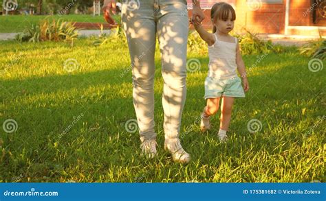 Little Daughter And Mother Holding Hands Are Walking In Park On Lawn