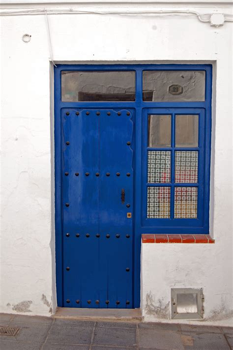 A Blue Door With Glass Panes On The Side Of A White Wall And Brick Floor