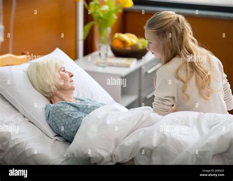 Side View Of Girl Visiting Sick Grandmother Lying In Hospital Bed Stock