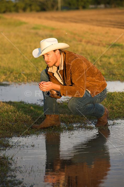 Cowboy Kneeling Down To Gather Water From A Pond On A Ranch Rob Lang