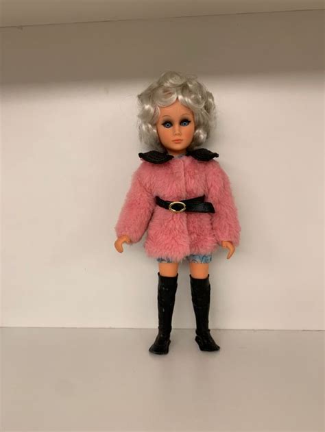 A Doll In A Pink Fur Coat And Black Boots Standing On A White Surface
