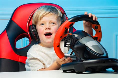 Cute Blond Boy In Headphones With Steering Wheel Play Race Game Stock