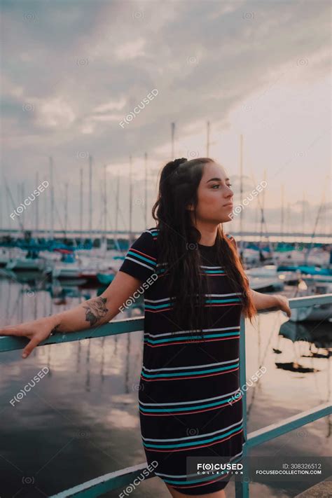 Happy Young Tattooed Woman In Dress Standing On Wharf Filled With
