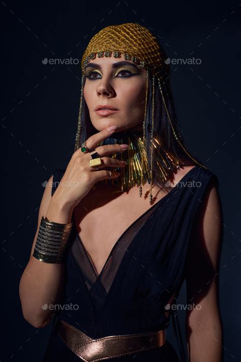 Portrait Of Woman In Egyptian Headdress And Costume Touching Chin While Standing On Blue