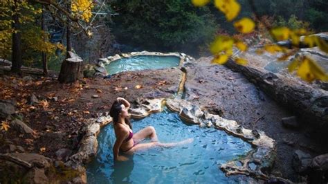 A Woman Sitting In A Hot Tub Surrounded By Rocks And Trees With Fall