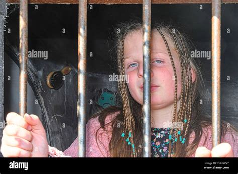 Sad little girl behind iron bars. Little girl behind the bars. Violence