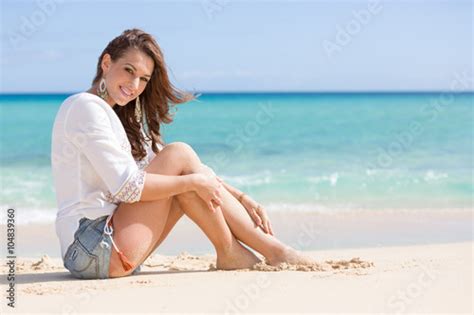 Junge Hübsche Frau In Jeans Hot Pants Sitzt Am Strand Vor Blauem Ozean Stockfotos Und