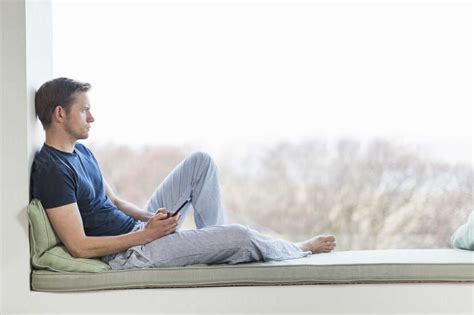 Mid Adult Man Sitting On Window Seat Looking Out Of Window Stock Photo