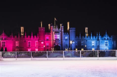 An Ice Rink In Front Of A Castle Lit Up With Pink And Blue Lights At Night
