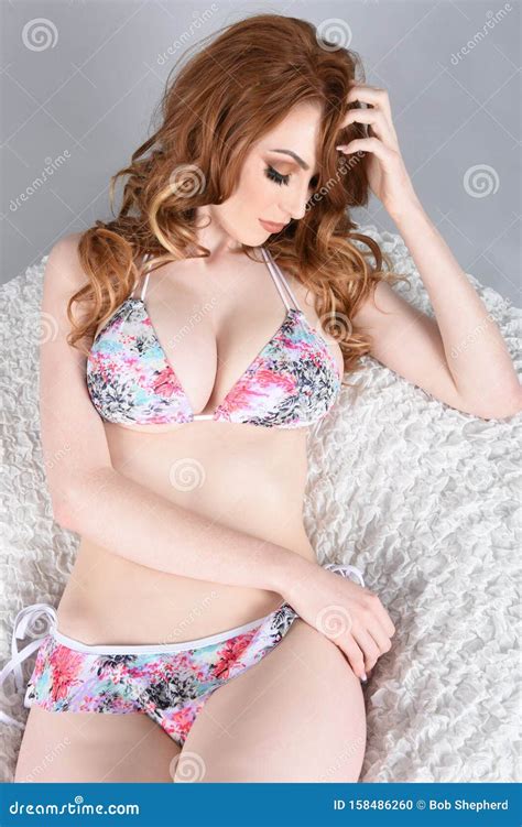 Sexy Busty Redhead On A White Cushion Dressed In A Flowery Bikini