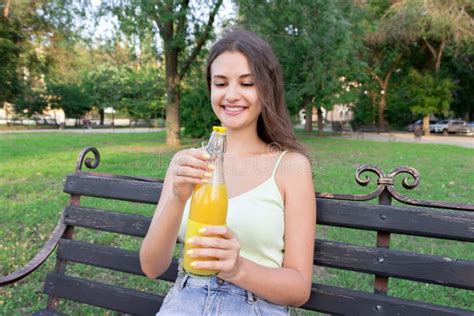 Beautiful Woman Is Opening A Bottle Of Fresh Cold Juice On The Bench In The Park In Hot Summer