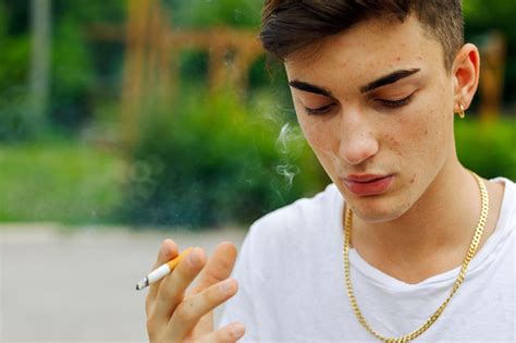 Young Man Smoking A Cigarette Outdoors Exhaling A Puff Of Smoke Stock