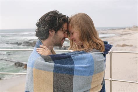 caucasian couple wrapped in blanket standing at promenade near beach
