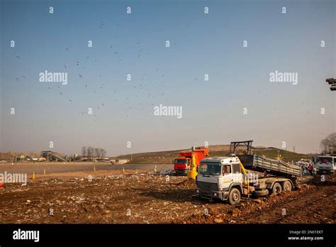 Municipal Waste Landfill Workers With Trucks And Bulldozers At Work In