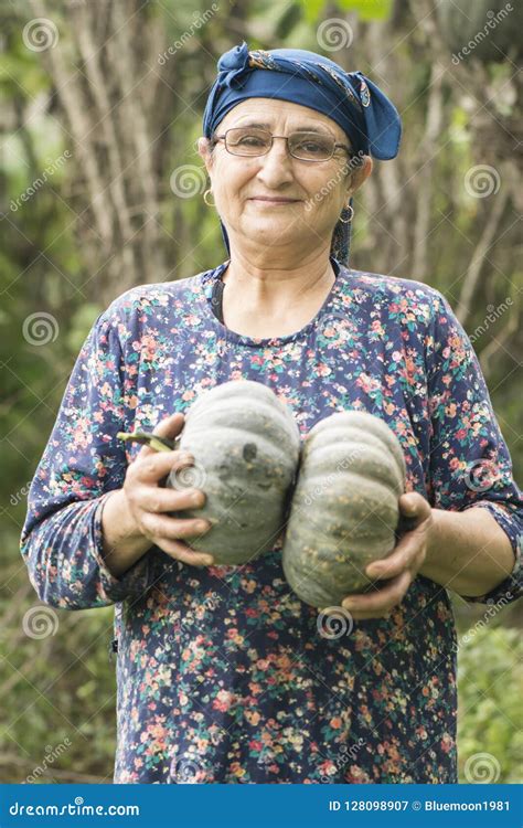 Happy Old Woman Farmer Holding Pumpkins In Hands At Green Farm Stock
