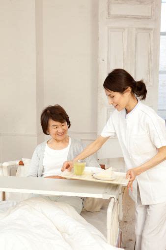 Female Caregiver Serving Meals For Senior Woman In Bed Caregiver