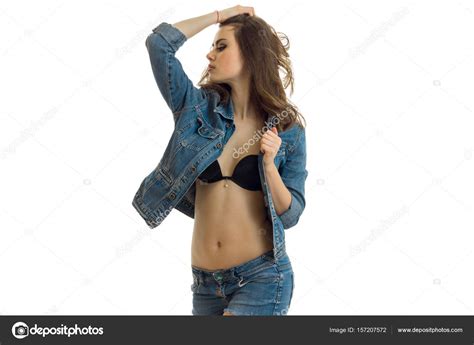 Hot Sexy Brunette In Jeans Clothes Stands In The Studio And Kept The Ball For Hair Stock Photo