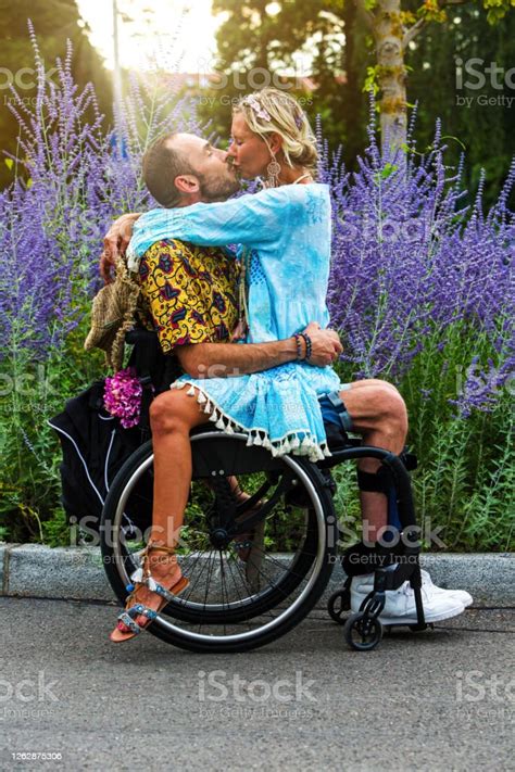 Young Man In Wheelchair With Woman Sitting On His Lap And Kissing Him