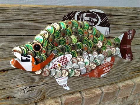 A Fish Made Out Of Beer Bottle Caps Sitting On Top Of A Wooden Plank Wall