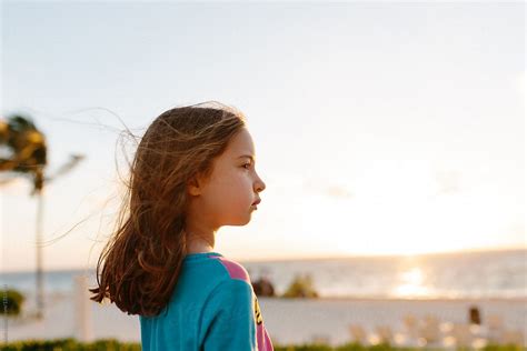 Cute Young Girl Enjoying The Wind Blowing In Her Face On The Beach By