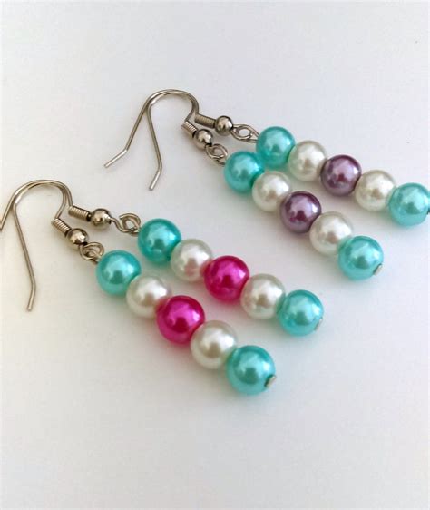 Three Pairs Of Colorful Pearls Are Hanging From Silver Hooks On A White