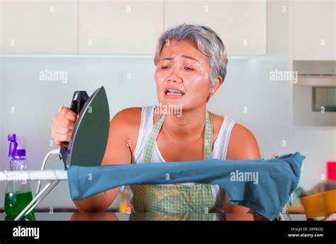 Desperate And Stressed Middle Aged Asian Woman Ironing In Stress At Home Kitchen Feeling