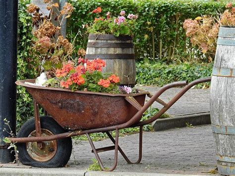 A Wheelbarrow With Flowers In It Sitting On The Side Walk Next To A Pole