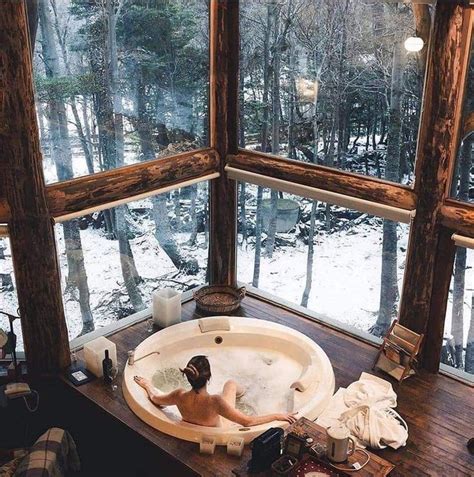 A Woman Is Sitting In The Bathtub Looking Out At The Snow Covered Forest Outside