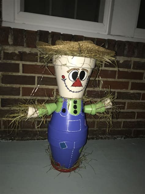 A Ceramic Scarecrow With Straw On Its Head And Eyes Standing In Front