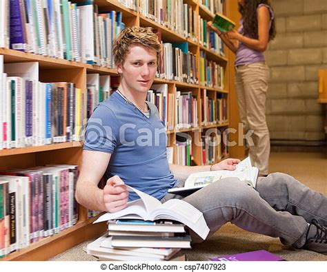 Male Student Doing Research While His Classmate Is Reading In A Library