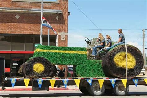 People Are Riding On The Back Of A Tractor Decorated With Grass