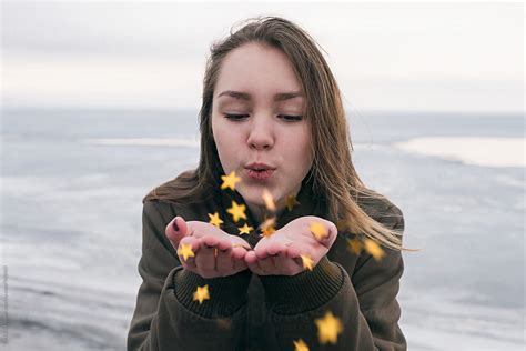 Close Up Of Young Woman Blowing On Golden Stars In Hands By Stocksy