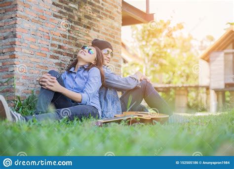 Hipster Man Playing Guitar For His Girlfriend Outdoor Against Brick Wall Enjoying Together