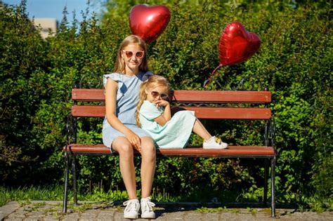 Premium Photo Two Beautiful Young Girls In Sun Protected Glasses Sit On A Park Bench