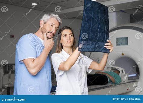 Doctors Examining X Ray With Patient Lying On CT Scan Machine Stock