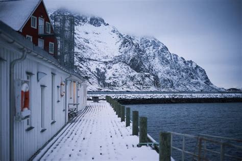 Typical Scandinavian House At Fjord In Front Of Snow Covered Mountains