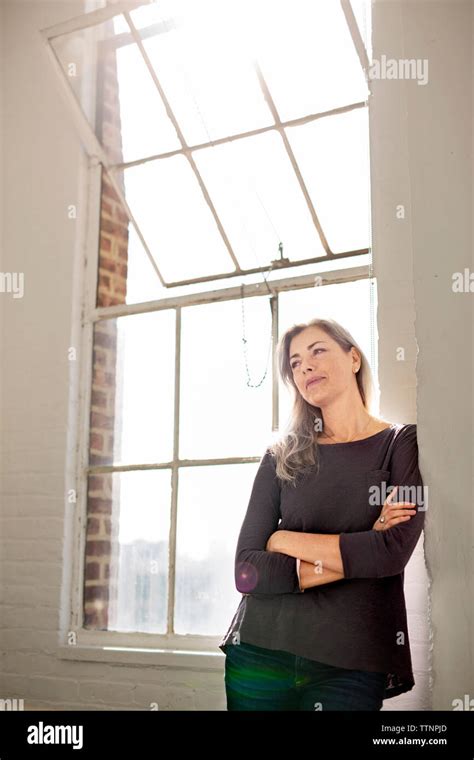 Thoughtful Woman With Arms Crossed Leaning On Wall At Home Stock Photo