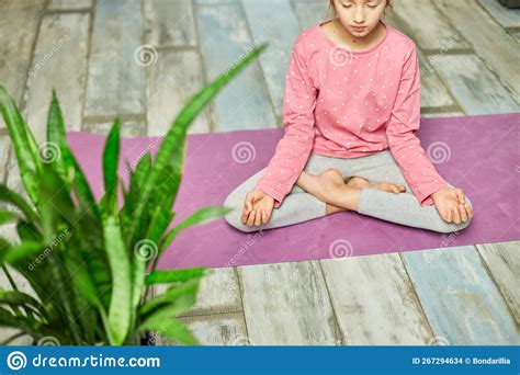 Cute Little Girl Sitting On Fitness Mat In A Lotus Position While Doing