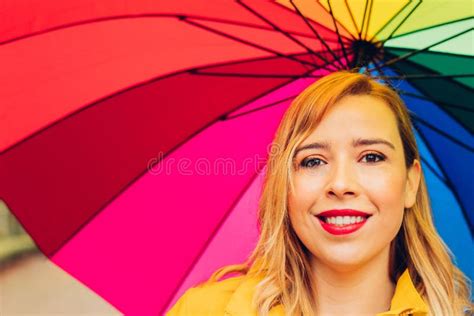 Young Adult Woman 30s Holding A Multicolored Umbrella On A Rainy Day Looking At The Camera With