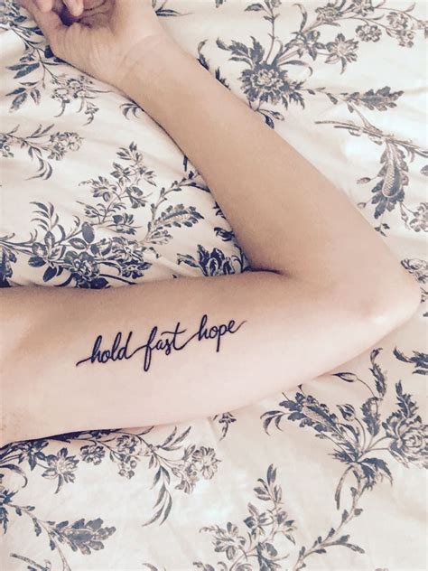 A Woman Laying On Top Of A Bed With Her Arm Tattoo Reading Hold Fast Hope