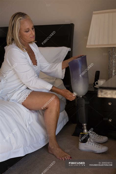 Mature Woman Holding Prosthetic Leg In Bedroom At Home