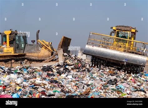 Municipal Waste Landfill Workers With Trucks And Bulldozers At Work In