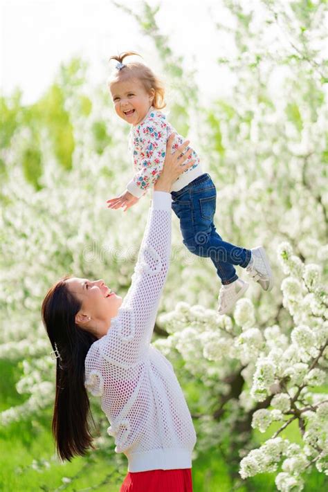 Mom Throws Up Her Daughter In The Park By A Flowering Tree Happy