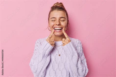 Young Glad Woman Points At Toothy Smile Shows Perfect White Teeth Being In Good Mood Keeps Eyes