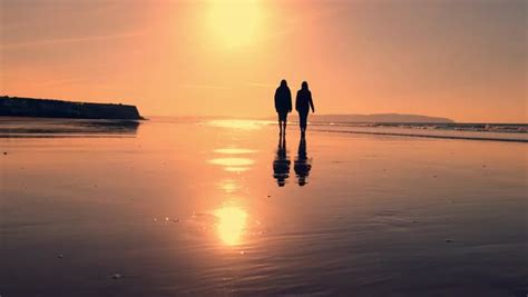 Two People Walk On A Sandy Beach At Sunset Stock Video Footage Dissolve