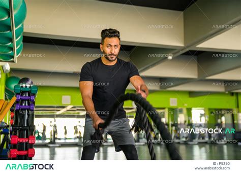 مدرب عربي خليجي سعودي يقوم بالتمرن على الحبل الثقيل في صالة الرياضة ، ممارسة التمارين رياضية في
